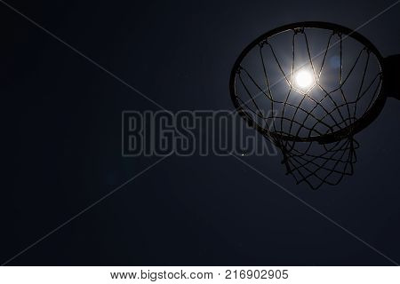 Looking up through silhouetted basketball goal to the moon at night