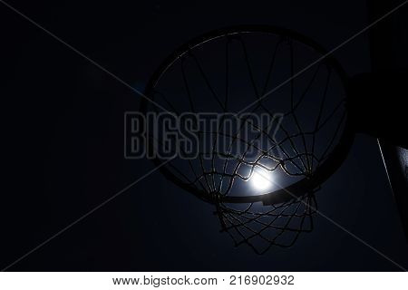 Looking up through silhouetted basketball goal to the moon at night