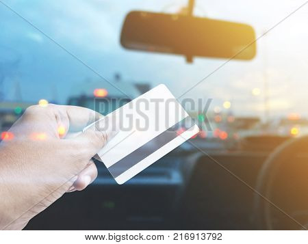 Hand holding credit card over blurred background of car cockpit at pay toll station on tne traffic jam evening.
