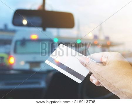 Hand holding credit card over blurred background of car cockpit at pay toll station on tne traffic jam evening.