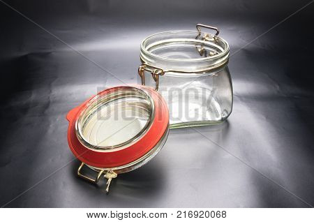Empty glass jar with the open cap hold with metal wire over the black background