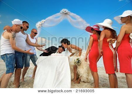 Mariée et le marié sous l'arche sur la plage en train de prendre une bouchée de gâteau de mariage.