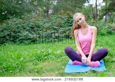 Beautiful sport woman doing stretching fitness exercise in city park at green grass.
