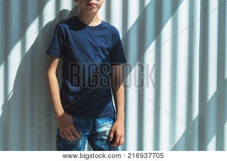 Front view. Young hipster boy in sunglasses dressed in black t-shirt is stands indoor against white wall. Mock up. Space for logo, text, image.
