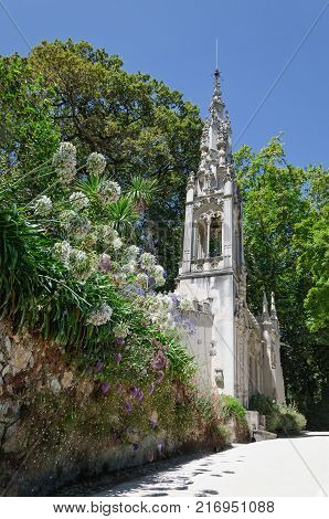 Beautiful white chapel among blooming flowers in green park of UNESCO World heritage site "Quinta da Regaleira". It is one of the main tourist attractions in Sintra Portugal.
