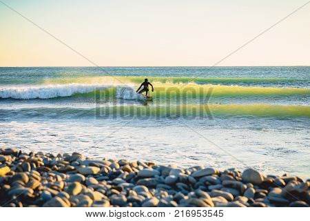 Surfing on ocean wave at sunset or sunrise. Winter surfing in wetsuit