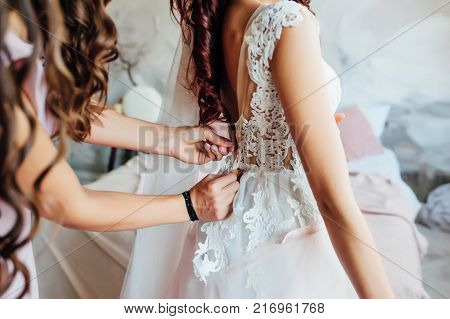 Bridesmaid preparing bride for the wedding day, helping fasten her dress