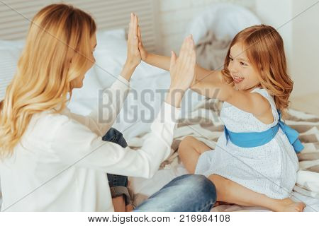 Pleasant motherhood. Happy cheerful positive mother and daughter sitting together and having fun while playing a clapping game