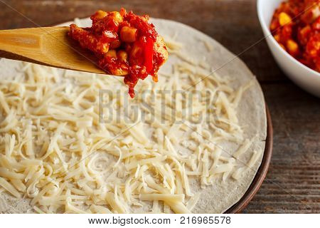 making of quesadilla. Wooden spoon spread the filling on the tortilla sprinkled with cheese.