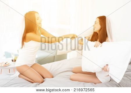 Pre-wedding care. Girls at a hen-party. Girls are having pillow fight on the bed. They have fun in a bright room.