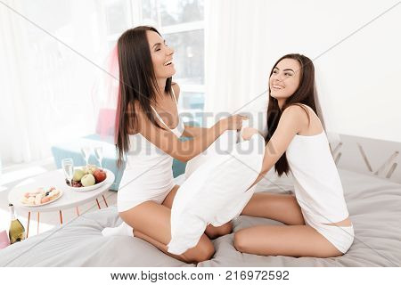 Pre-wedding care. Girls at a hen-party. Girls are having pillow fight on the bed. They have fun in a bright room.