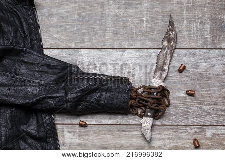 The big knife is wrapped in chains of a jacket as if the silhouette is holding a knife next to bullets on a wooden floor
