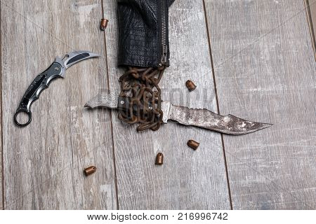 A rusty knife in chains of a jacket is like a hand next to bullets and a knife on a wooden table. View from above