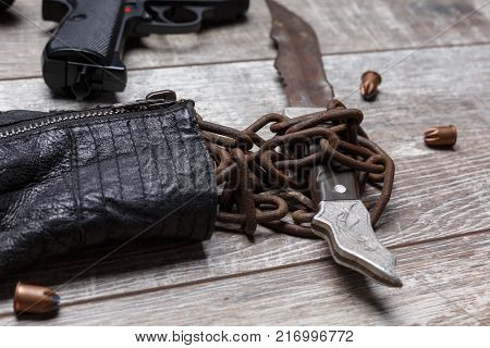 Rusty knife in chains of a jacket close-up next to bullets and a gun on a wooden background