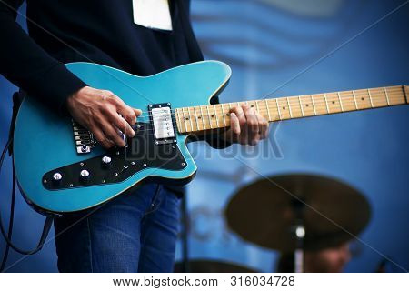 A Rock Musician In A Black Hoodie And Blue Jeans Plays A Cool Track On A Blue Six-string Electric Gu