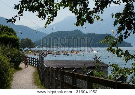 Lake Como, Italy - July 21, 2019. Summer Activities On A Beach In Mountain Lake - Cycling, Windsurfi