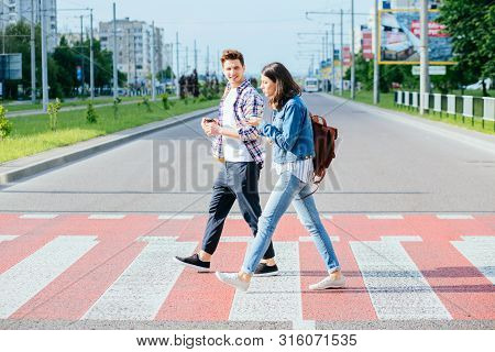 A Picture Of A Happy Young Couple Students On A Walk On A Day Off. A Happy Friends Crosses The Road 