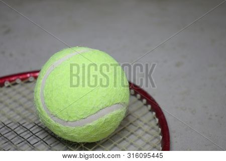 Tennis Ball On Racket On Grey Surface.