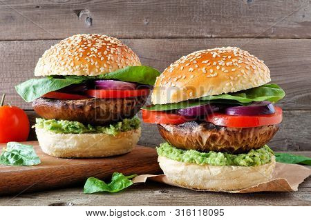 Portobello Mushroom Meatless Burgers With Avocado, Tomato, Spinach And Onion Against A Dark Wood Bac