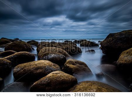 Creative Longtime Photo Over A Rock Beach With Fantastic Clouds On The Sky