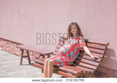 The Pregnant Girl Basks In The Sun. The Concept Of Warm Leisure - A Beautiful Pregnant Girl With Lon