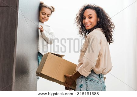 African American Woman With Box In Hand Standing On Stairs While Daughter Looking Down