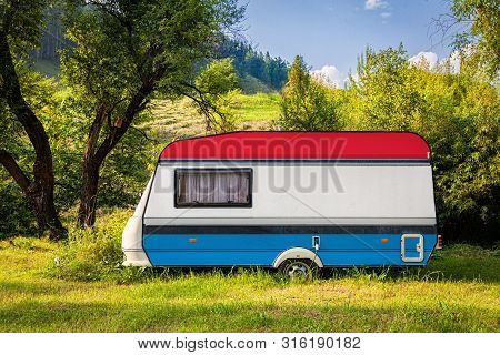 A Car Trailer, A Motor Home, Painted In The National Flag Of  Luxembourg Stands Parked In A Mountain
