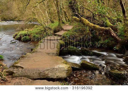 Long Exposure Of The River Flowing Under A Bridge At Tarr Steps In Devon