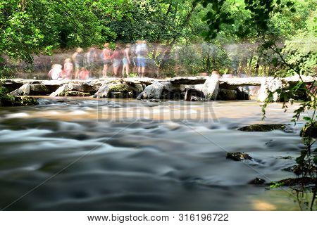Long Exposure Of The Bridge At Tarr Steps In Devon With Lots Of People On It On A Bank Holiday Monda