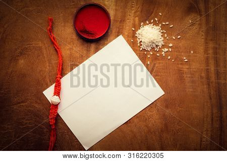 Top View Of Rakhi On A Wooden Table With Kumkum, Chawal Or Rice Grains And A White Paper For Copy Sp