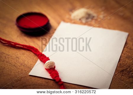 Closeup Shot Of Handmade Rakhi Or Threads On A Wooden Surface With Kumkum, Chawal And White Paper Fo