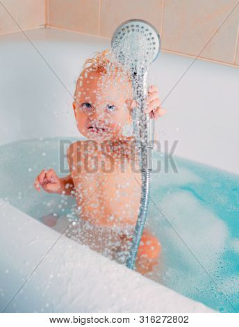 Cute Baby In Soft Bathrobe After Bath Playing In Kids Room. Pleasant Little Kid Playing In Bath Tube