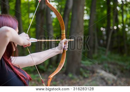 Woman Archer Shooting Targets With Wooden Bow At Historical Festival. Archery And Medieval Culture C