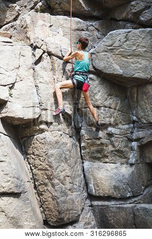 The Girl Climbs The Rock. Rock Climber Is Training On Natural Terrain. Extreme Hobby. A Woman Overco