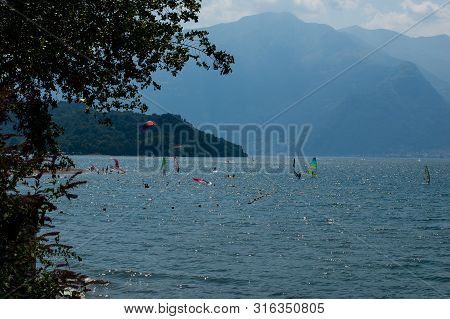 Lake Como, Italy - July 21, 2019: View Of Mountain Lake With Windsurfers Training On A Sunny Summer 