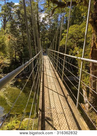 A Narrow Suspension Footbridge Spans Across A River In New Zealand Nobody In The Image