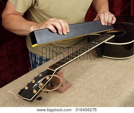 Musical Instrument Guitar Repair And Service - Worker Grinds Black Guitar Neck Frets.