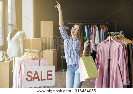 Young Caucasian Woman Dancing With Purchases At Showroom, Holding Credit Card, Sale Board