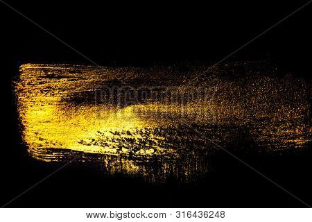 Creative brushstrokes of gold paint isolated on a black background. Gold paint texture.Acrylic gold paint. Smears of cosmetics, blush, highlighter, eye shadow, lipstick.