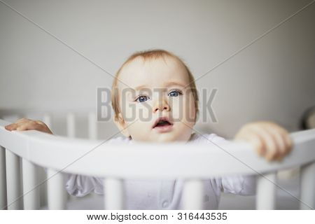 Adorable Baby Girl In Co-sleeper Crib Attached To Parents Bed. Little Kid Sitting In Cot