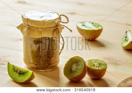 Handmade Green Healthy Kiwi Jam Glassjar With Raw Tropical Fruits On Wooden Table Background In Sun 