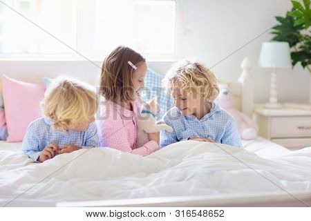 Kids Play In Bed. Children At Home In White Sunny Bedroom. Brother And Sister In Matching Pajamas Pl