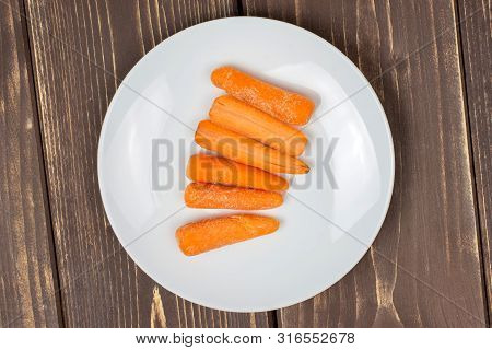 Lot Of Whole Stale  Orange Stale Baby Carrot Baby On White Porcelain Plate Flatlay Isolated On Brown
