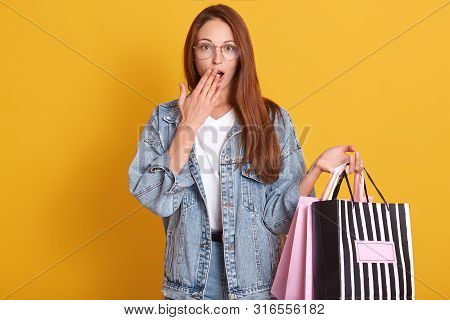 Photo Of Young Woman In Denim Jacket And Glasses Holding Shopping Bags Isolated Over Yellow Studio B