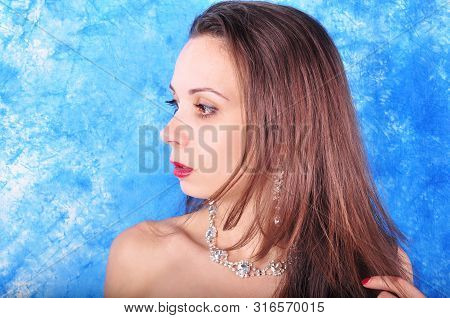 Dark-haired Girl In Exclavant Earrings And A Necklace On An Abstract Background
