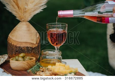 Rose Wine, Pouring From The Bottle Into The Glass Until Its Full. The Glass Is Standing Next To A Wo