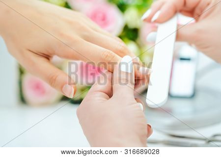 Close-up of the hands of a qualified manicurist filing the nails of a young woman in beauty parlor
