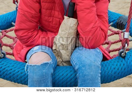 Girl Sitting On A Swing With A Bottle Of Alcohol, Close-up View