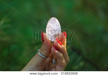 Female Hand With Red Manicure Holding Transparent Violet Amethyst Yoni Egg For Vumfit, Imbuilding Or