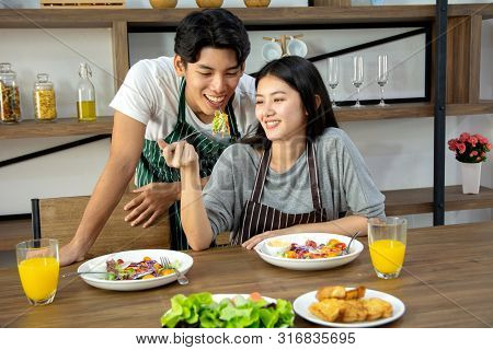 Portrait Of Cute Happy Couple In Aporn Jposting To Have Breakfast Decorated With Salad And Orange Ju